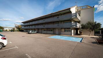 Un edificio de varios pisos con estacionamiento y un espacio reservado para personas con discapacidad, señalizado en azul.