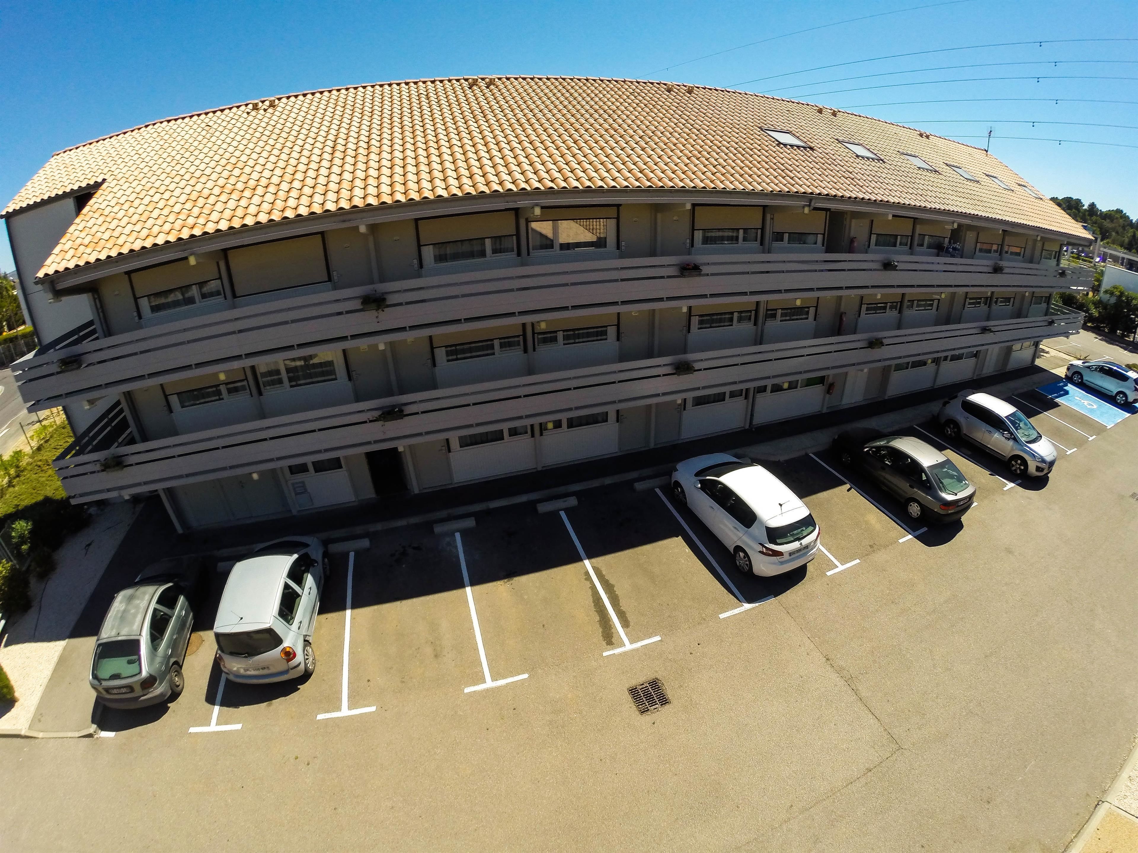 Un edificio de varios pisos con techo de tejas y un estacionamiento con varios automóviles.