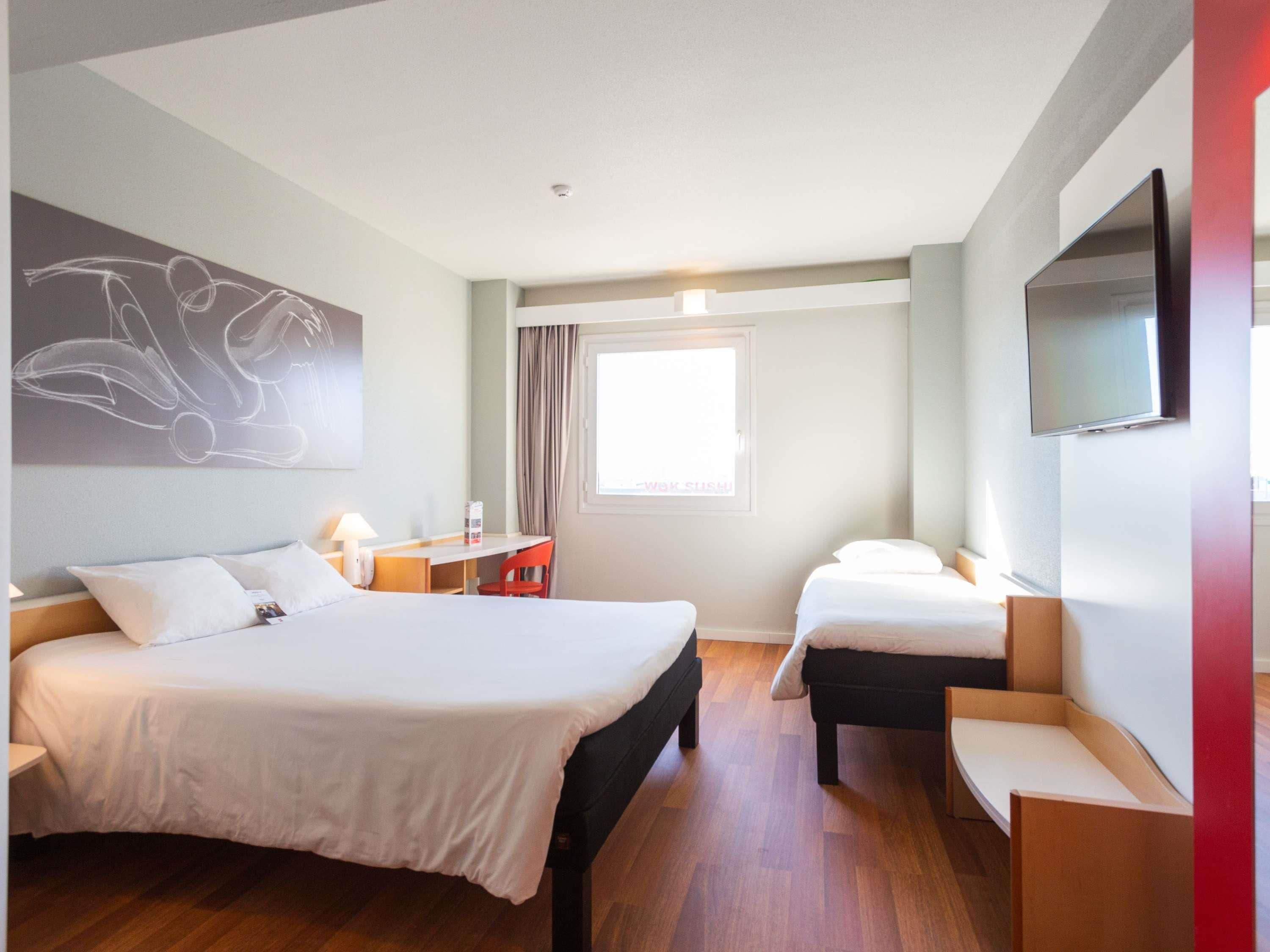 A hotel room with a bed, a desk, a chair, a TV, and a window.