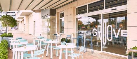 An outdoor seating area with tables and chairs, a covered walkway, and a building with large windows and a sign that reads 'GET INTO THE GRLOVE'.