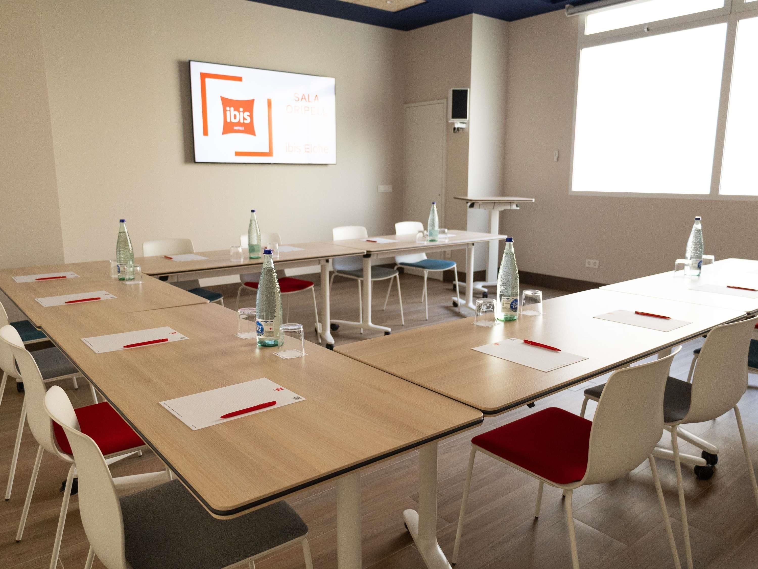 Ein Konferenzraum mit Tischen, Stühlen, Wasserflaschen und einem Schild an der Wand.