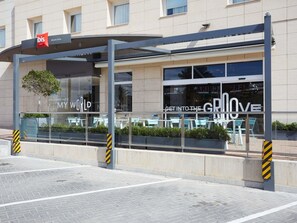 Una entrada de hotel moderna con un área de espera cubierta, ventanas de vidrio y asientos al aire libre.