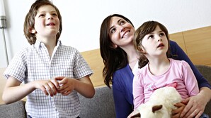 Drei Personen sitzen auf einer Couch, eine davon hält ein Stofftier.