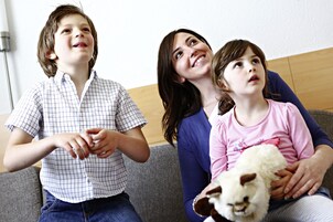 Three people sitting on a couch, one holding a stuffed animal.