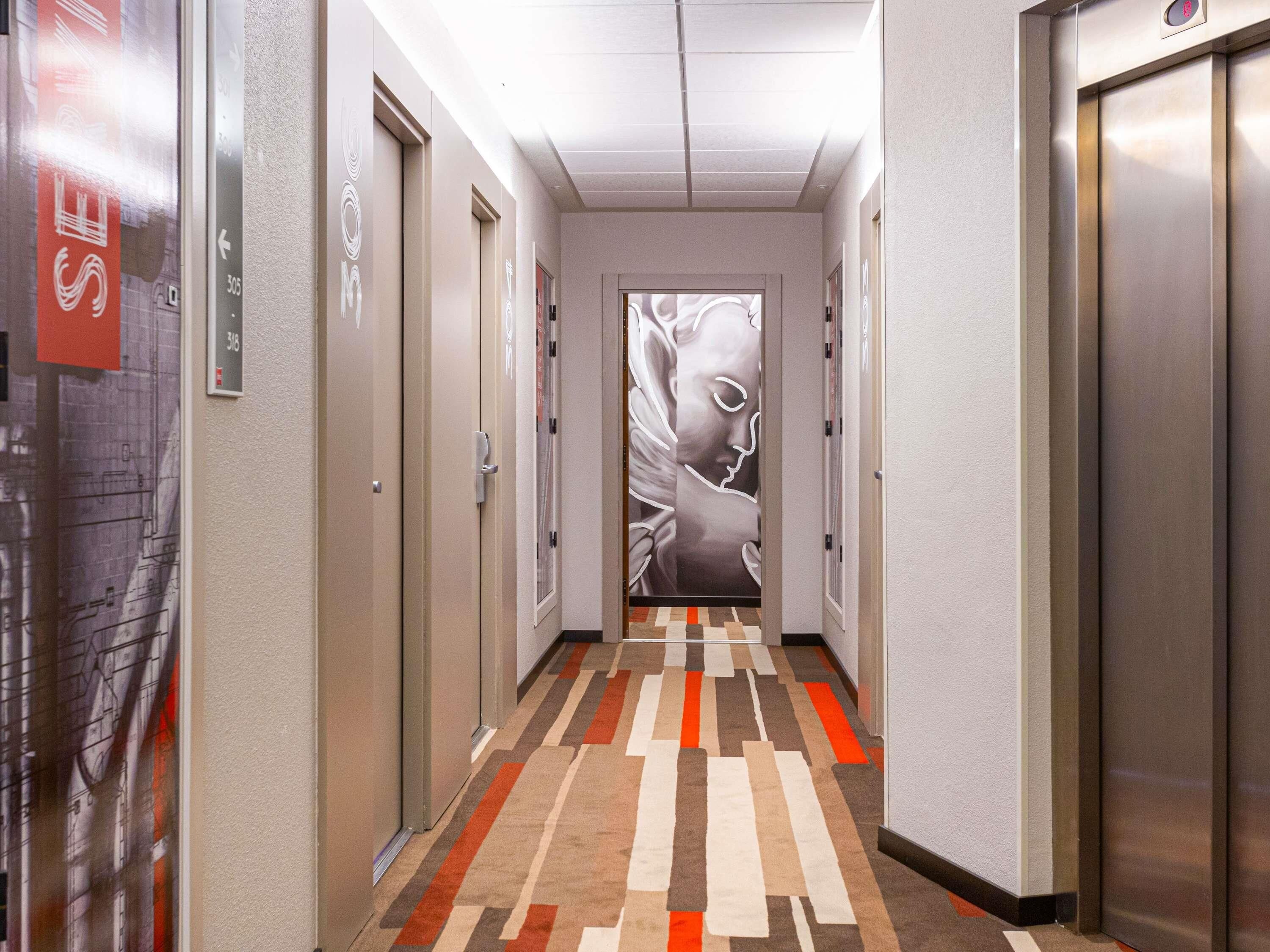 Un pasillo con puertas numeradas 305 y 316, un suelo con alfombra estampada y un mural en la pared.