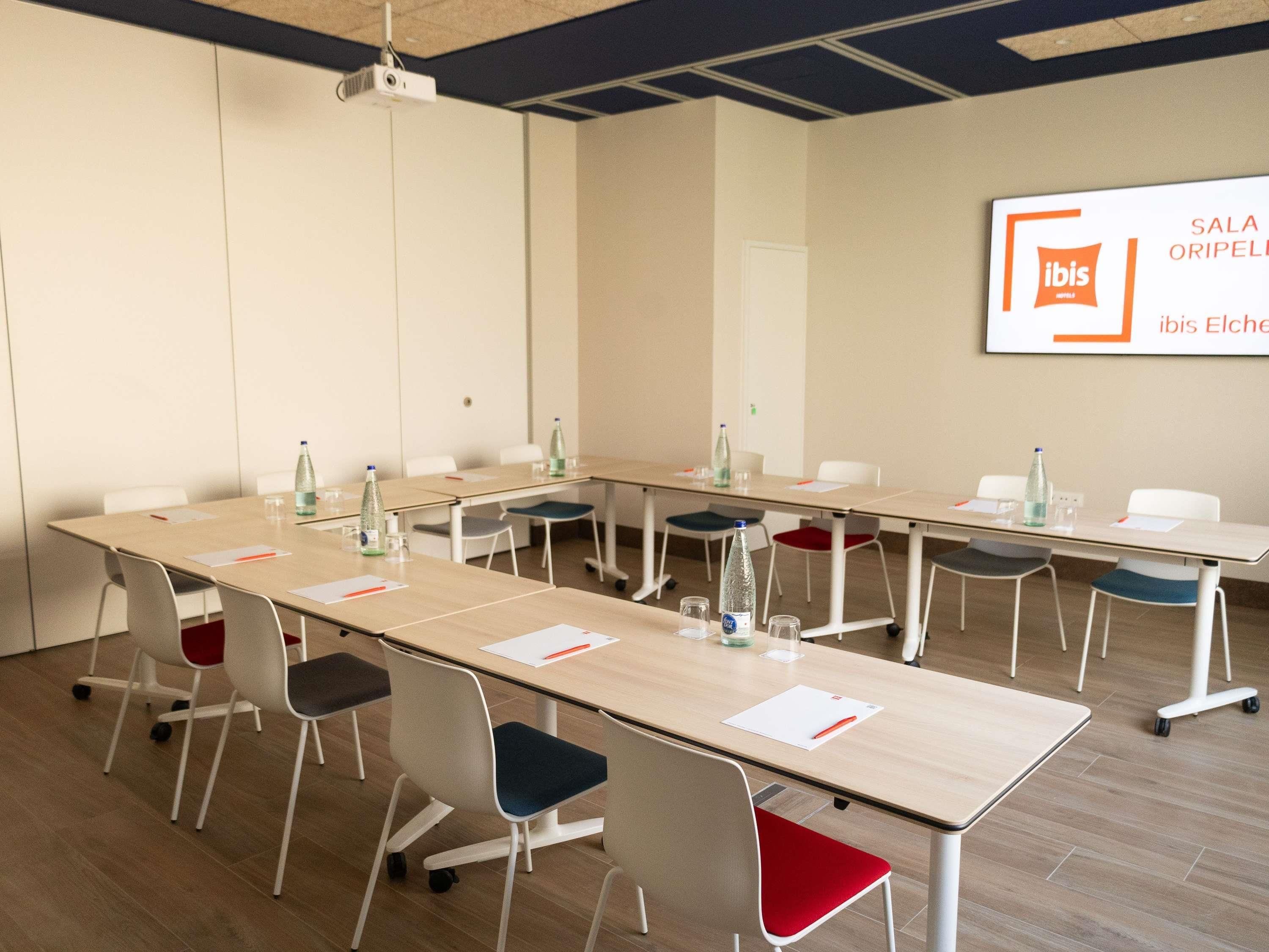 A conference room with a long table, chairs, a projector, and a sign on the wall.