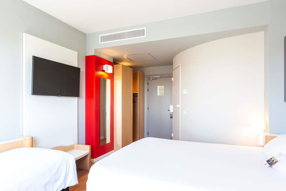A hotel room with a bed, a desk, a TV, and a door leading to a bathroom.
