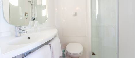 Un baño moderno con un lavamanos blanco, espejo y cabina de ducha con mampara de vidrio.