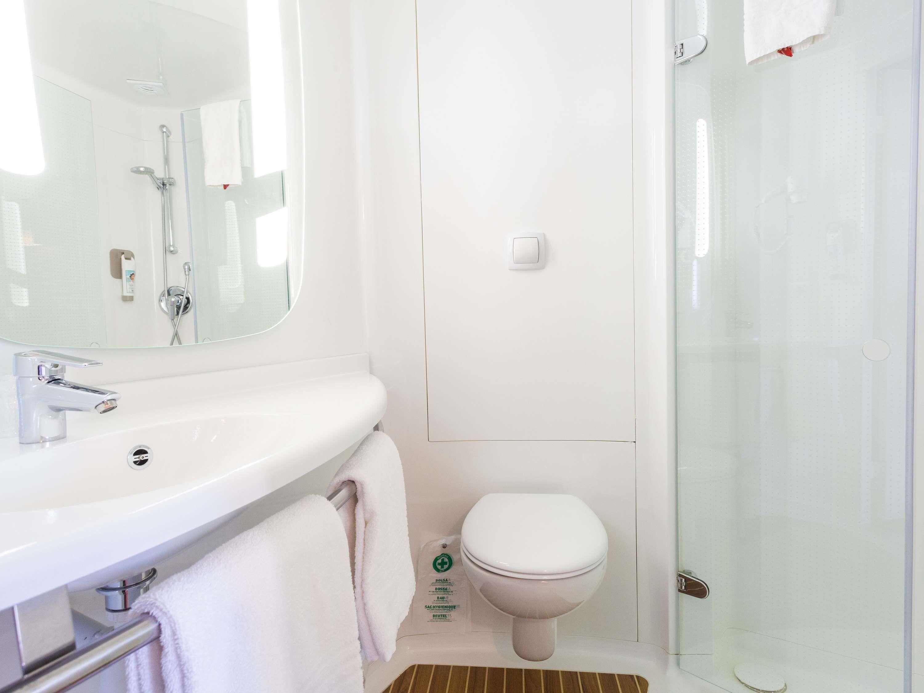 Une salle de bain avec un lavabo blanc, un miroir, des toilettes et une douche à parois de verre.