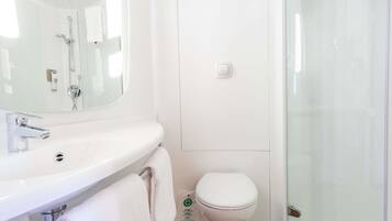 Une salle de bain avec un lavabo blanc, un miroir, des toilettes et une douche à parois de verre.