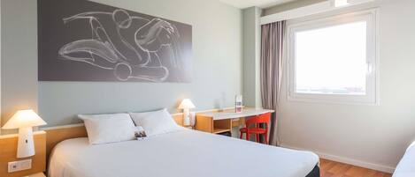 A hotel room with a bed, bedside lamps, a desk, a chair, and a window with curtains.