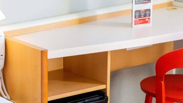 A white desk with a black trash bin underneath, a red chair, and a menu stand on the desk.