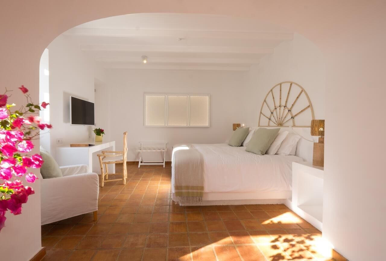 A bedroom with a bed, a desk, a chair, and a window with blinds.