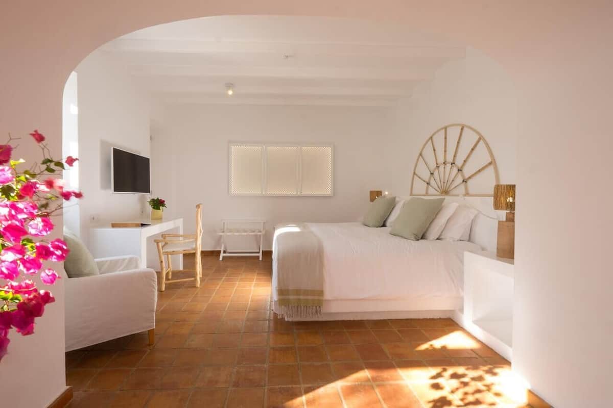 A bedroom with a bed, a desk, a chair, and a window with blinds.