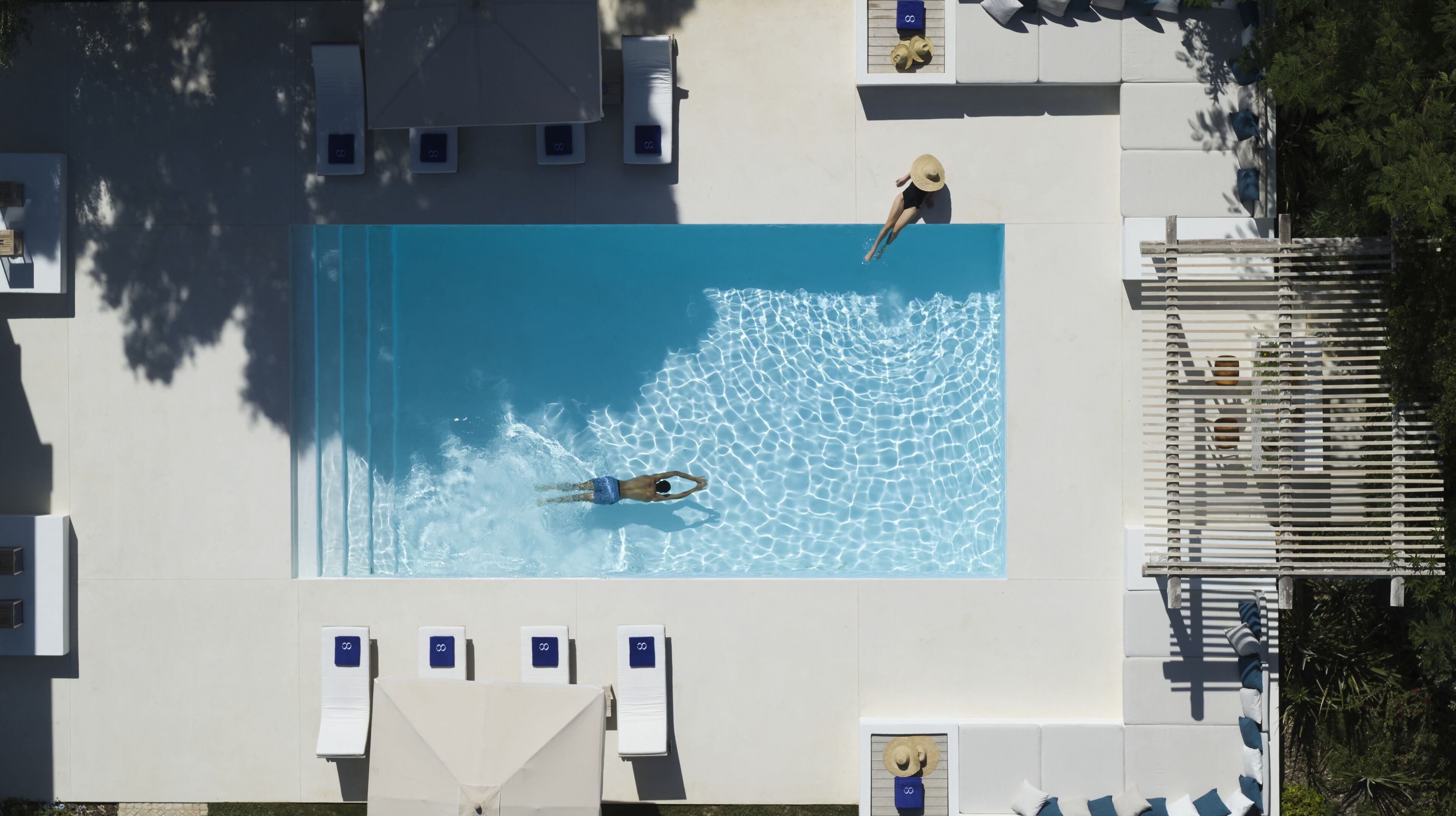 An aerial view of a swimming pool with clear water, surrounded by lounge chairs and umbrellas.