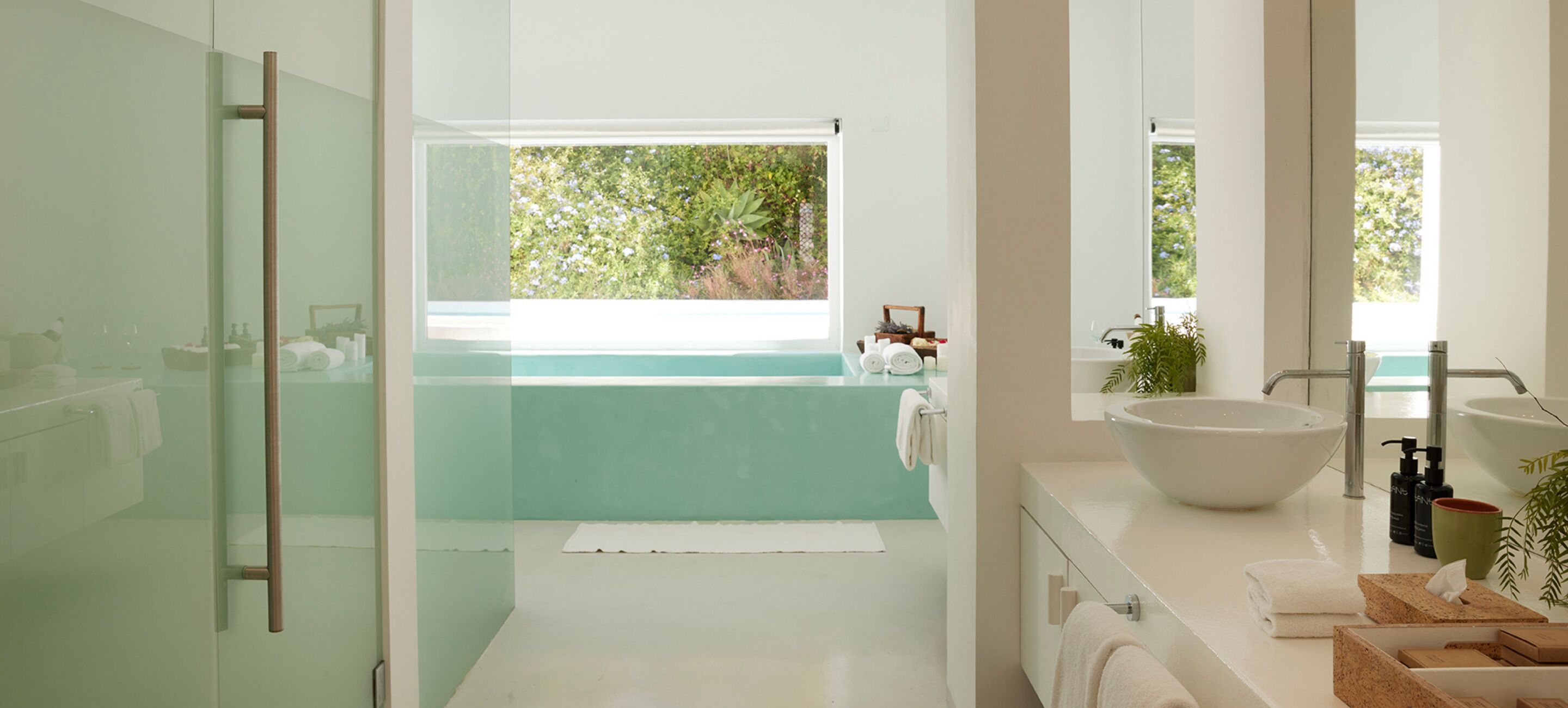 A modern bathroom with a glass shower enclosure, a large white sink, and a view of greenery outside.