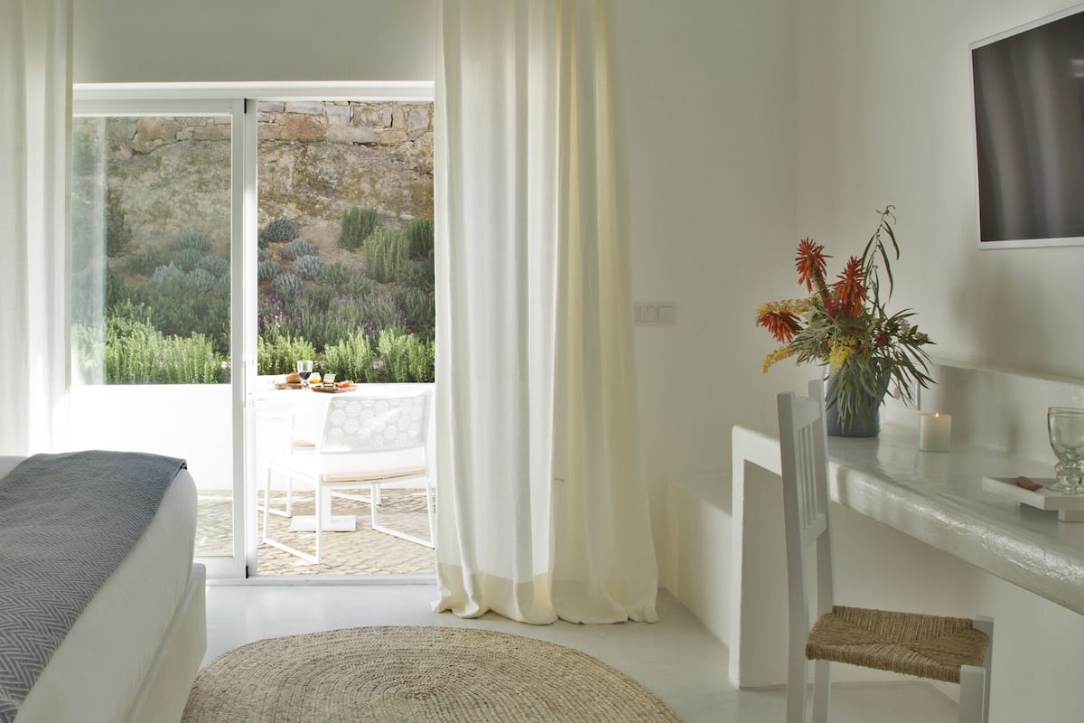 A bedroom with a bed, a desk with a vase, and a view of a garden through a sliding door.