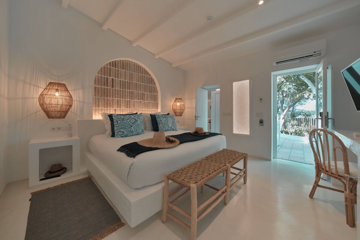 A modern bedroom with a large bed, bedside lamps, a bench, and a chair.