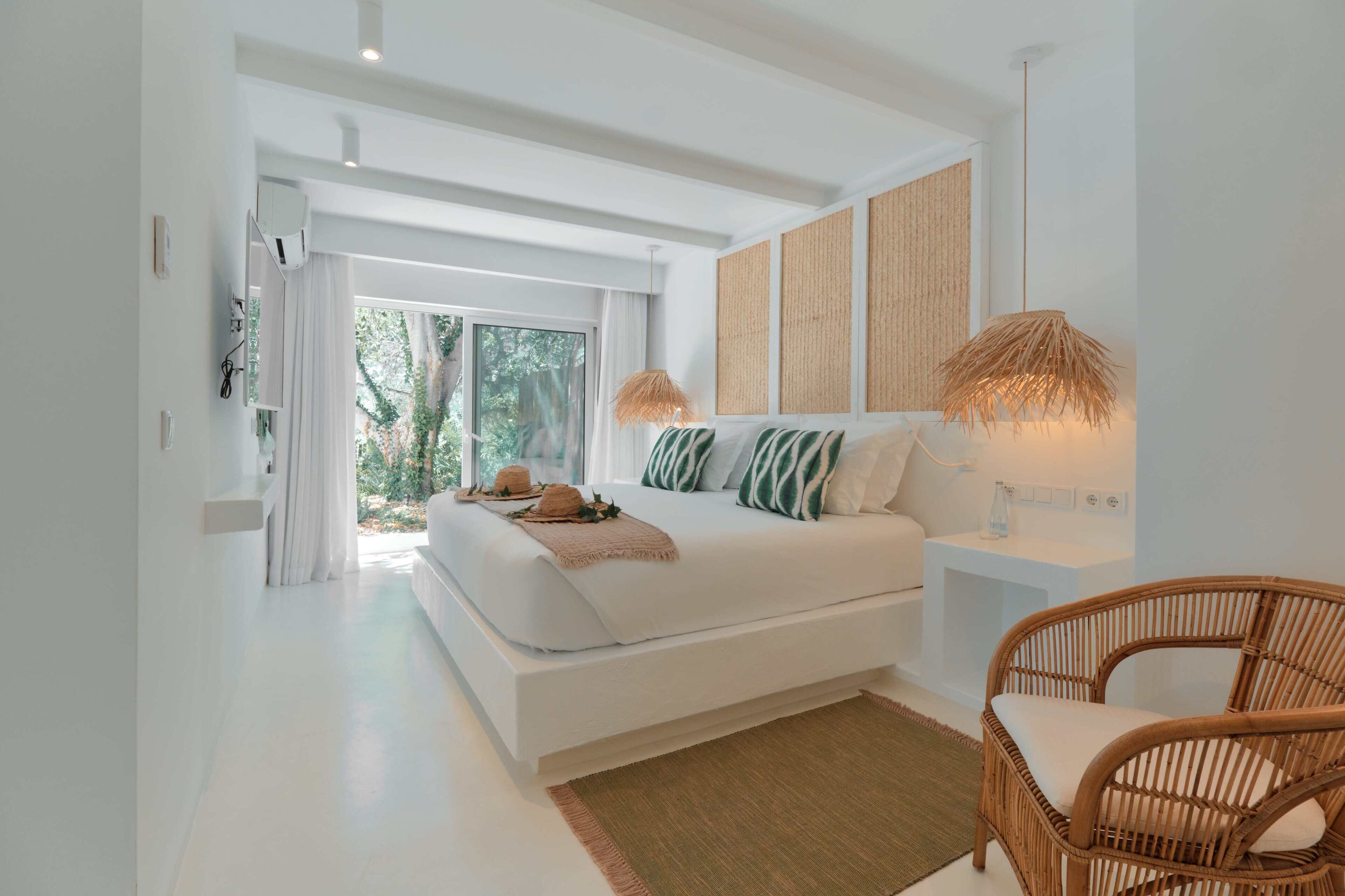 A modern bedroom with a large bed, a wicker chair, and a view of the outdoors.
