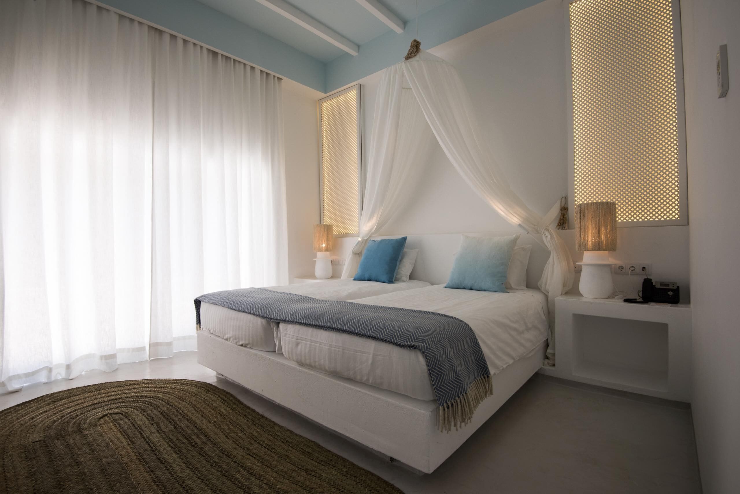 A modern bedroom with a bed, white curtains, a canopy, bedside lamps, and a rug.