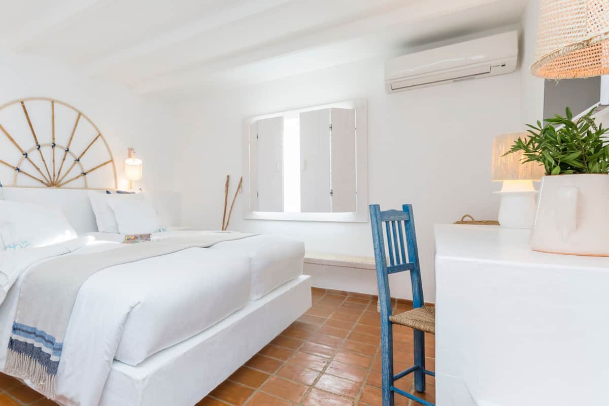 A bedroom with a bed, bedside tables, a chair, a window, and a potted plant.
