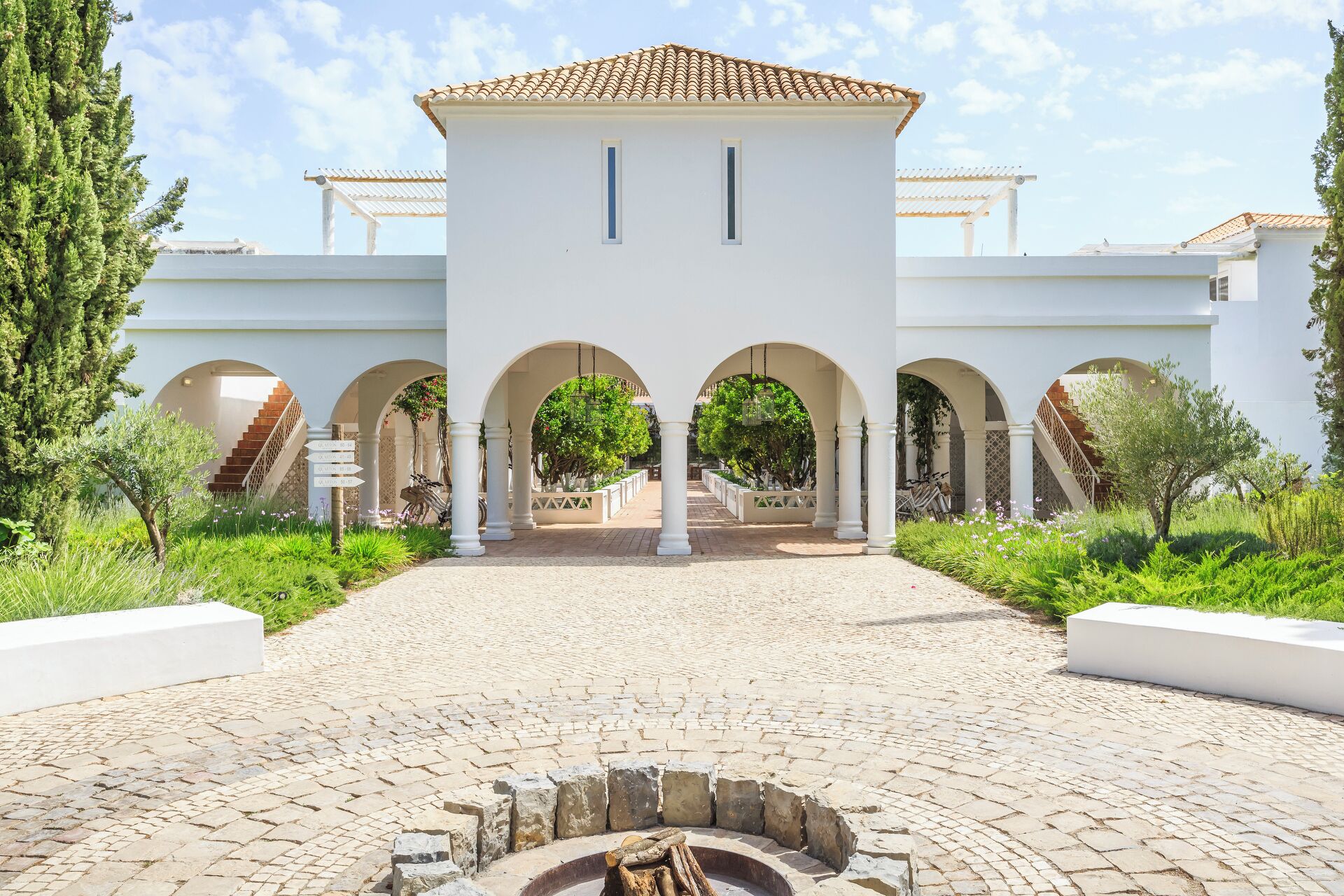 A courtyard with a central fountain, surrounded by white columns and arches, leading to a building with a tiled roof.