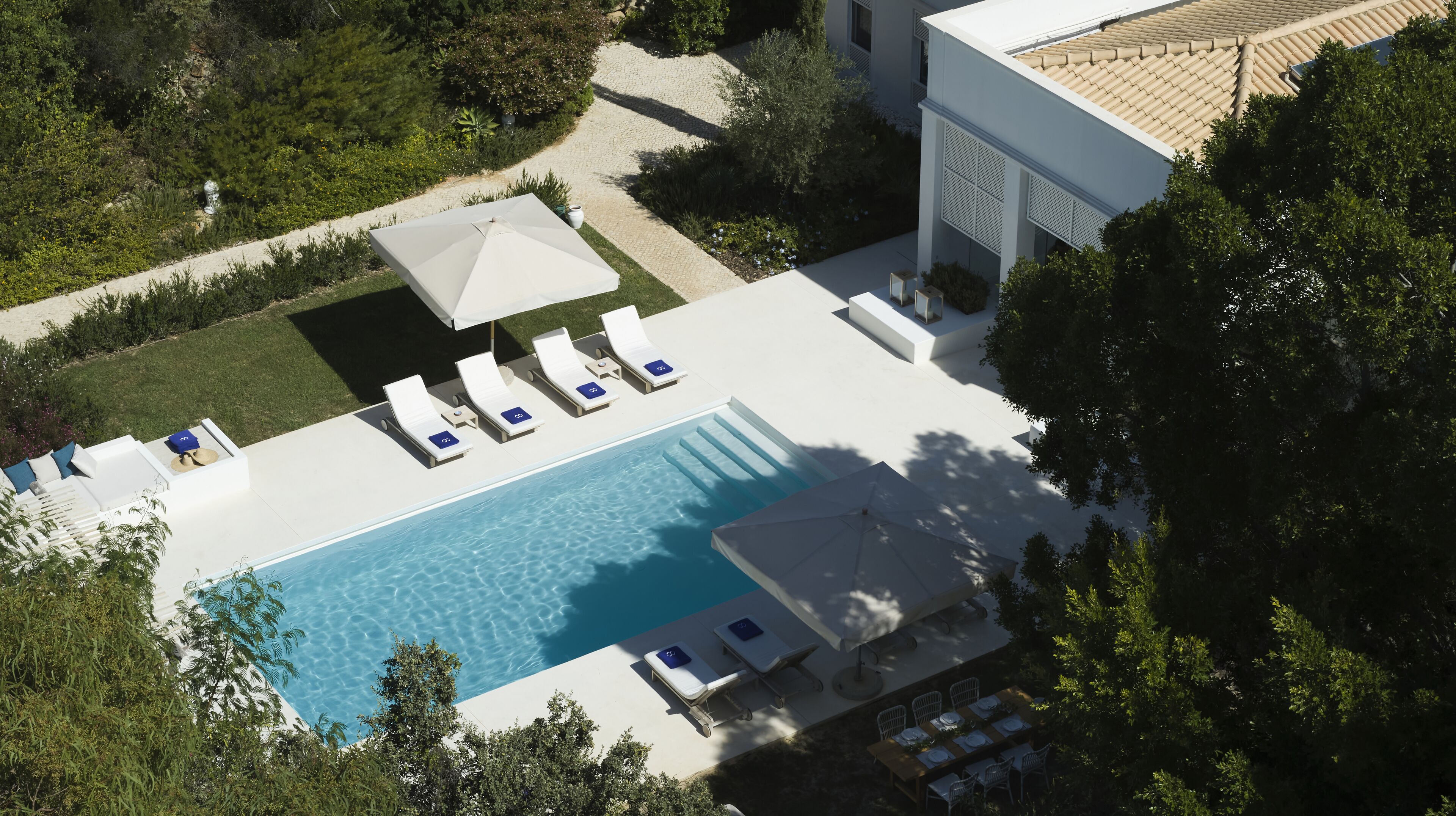 An aerial view of a modern hotel with a swimming pool, sun loungers, and a covered outdoor seating area.
