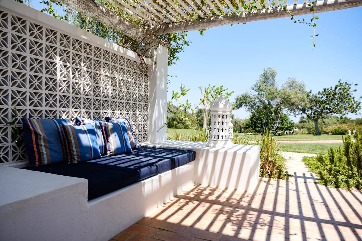 A sunlit outdoor seating area with a white lattice wall, a white lantern, and a garden path.
