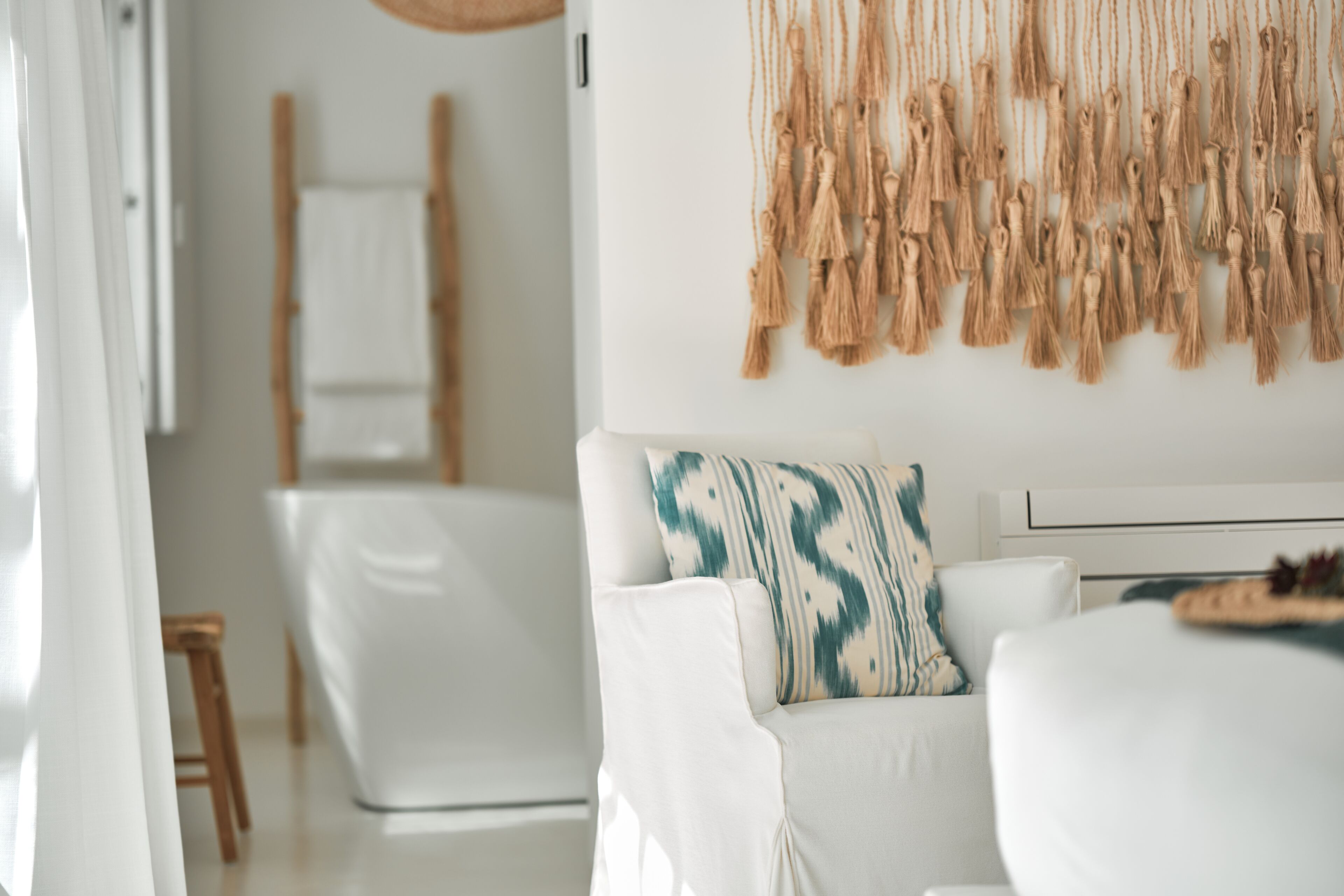Uma sala de estar moderna com um sofá branco, uma almofada decorativa estampada e um painel de parede em macramé.