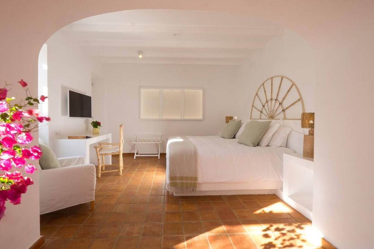 A bedroom with a bed, a desk, a chair, and a window with blinds.