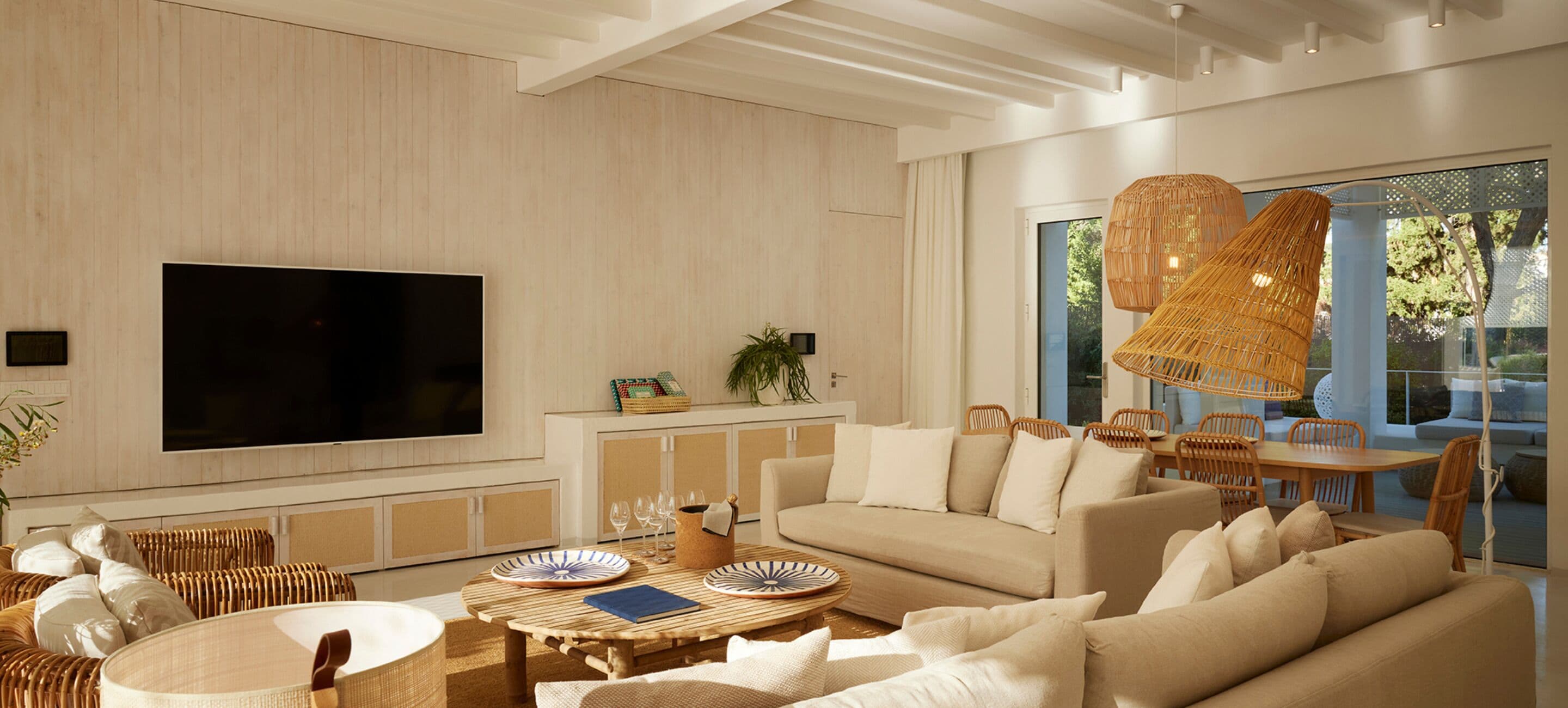 Una sala moderna con un televisor de pantalla plana grande, muebles de mimbre, un sofá y una zona de comedor con una mesa y sillas.