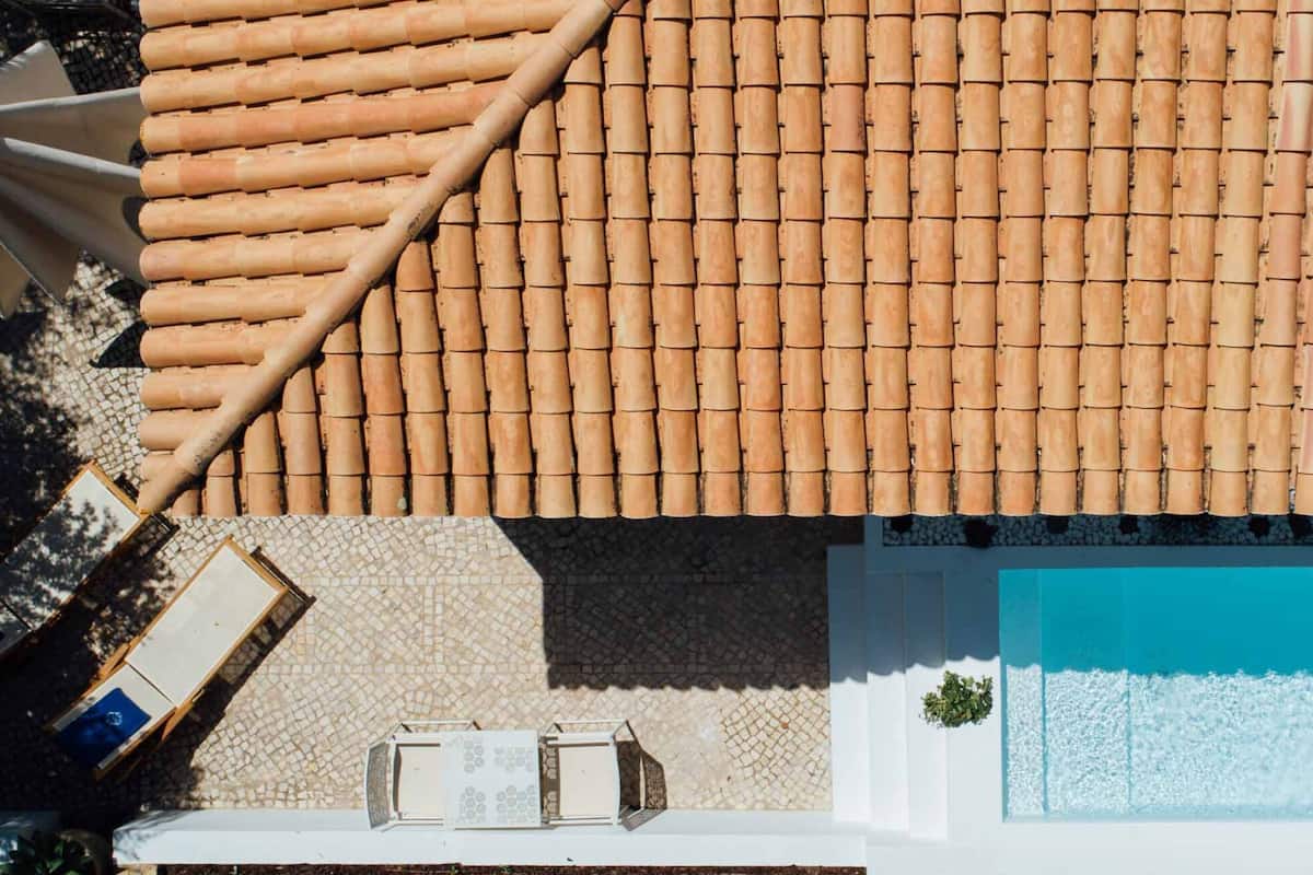 A rooftop terrace with a tiled roof, a swimming pool, and a seating area with a table and chairs.