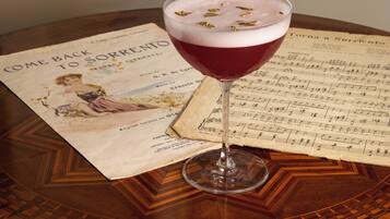 A glass of red beverage on a table with a sheet of music and a vintage poster.