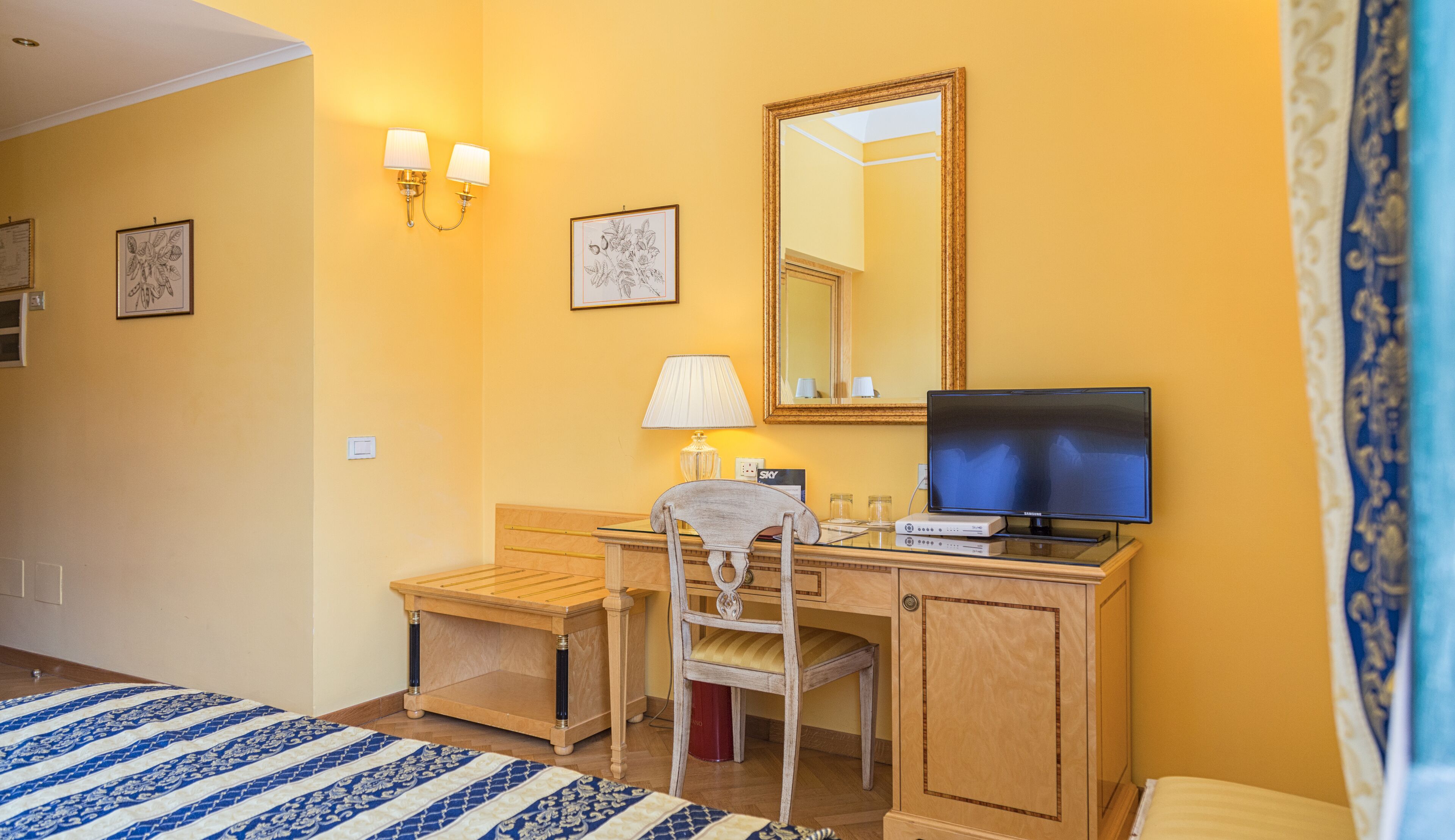 Ein Hotelzimmer mit Bett, Schreibtisch mit Stuhl, Fernseher, Lampe und Spiegel.