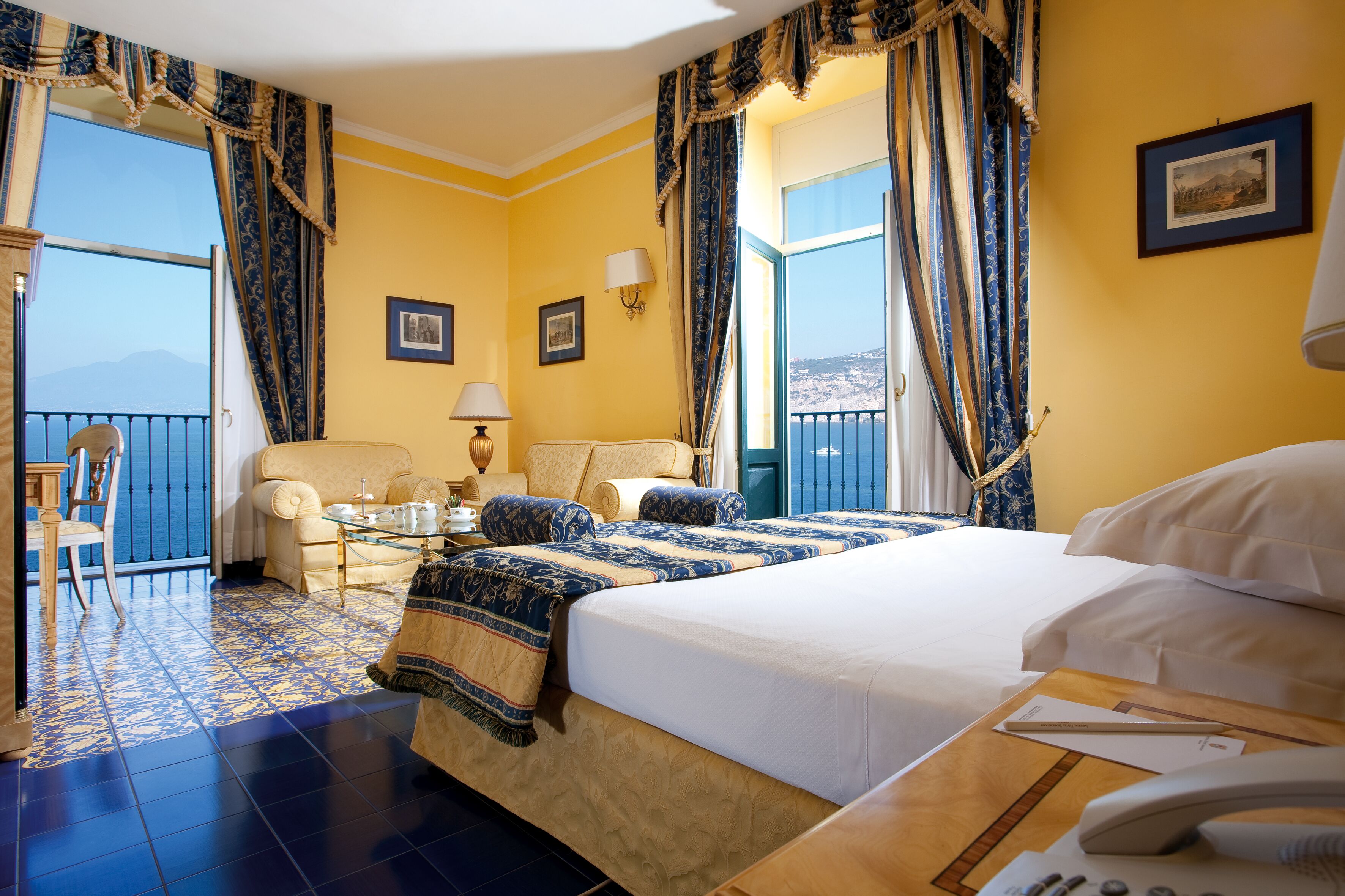A hotel room with a bed, a chair, a small table, and a balcony with a view.
