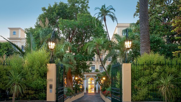 A gated entrance with a pathway leading to a building, surrounded by lush greenery and palm trees. - Imperial Hotel Tramontano (Sorrento)