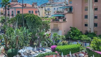 Una piscina sul tetto circondata da sedie a sdraio e ombrelloni, con edifici e una montagna sullo sfondo.