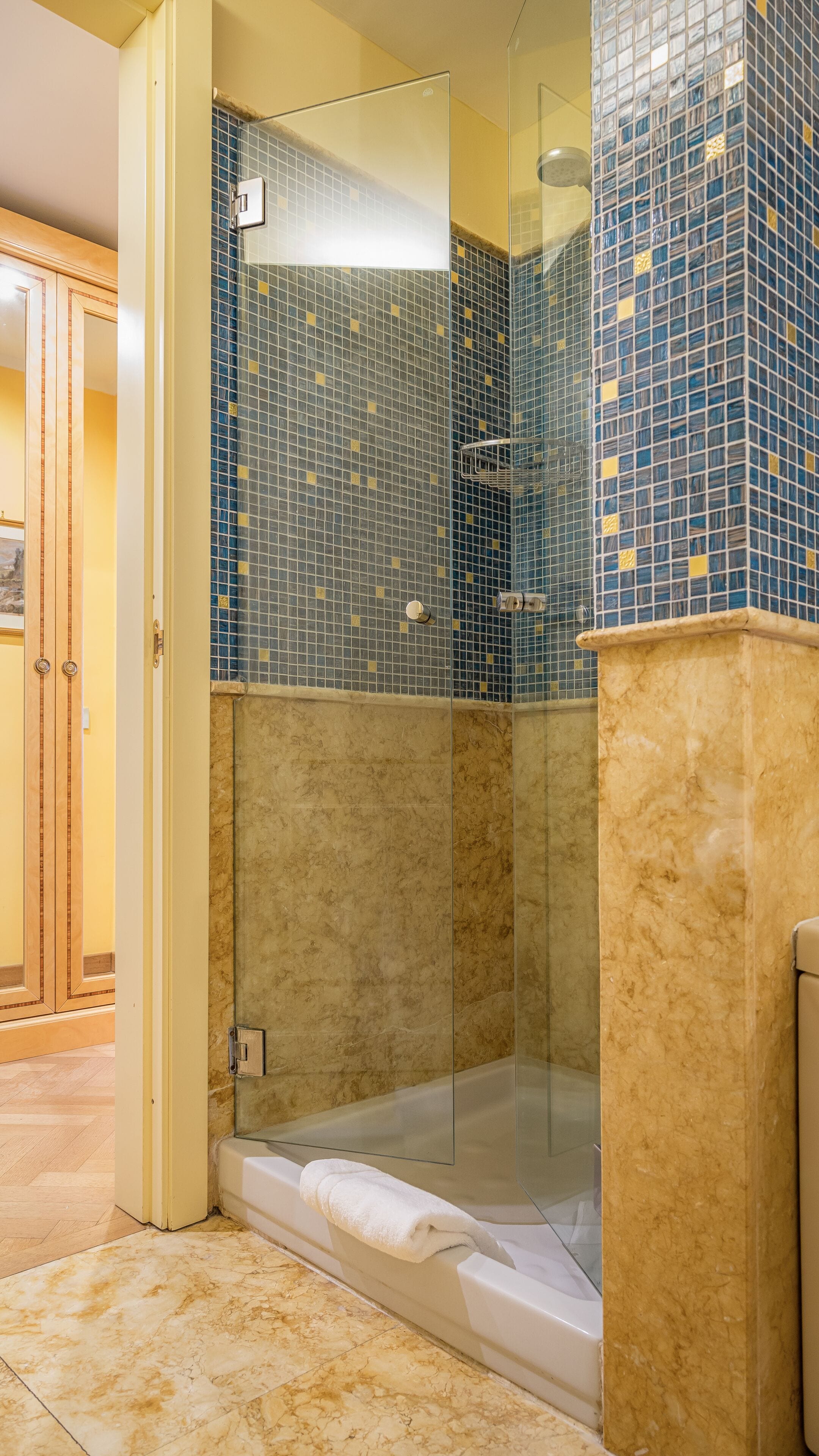 A glass-enclosed shower with a marble floor and a towel on the floor.