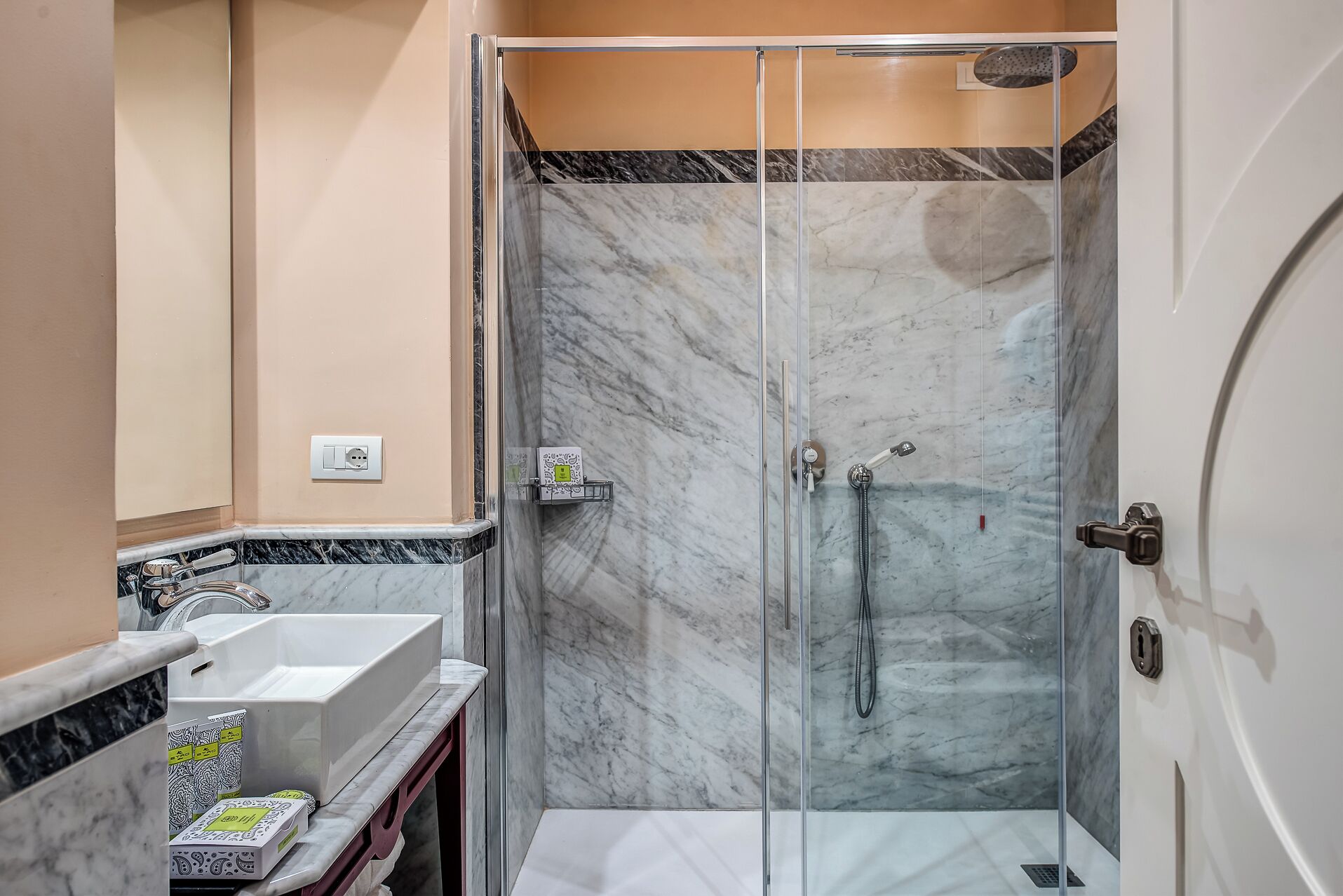 A modern bathroom with a glass-enclosed shower, a white sink, and marble flooring.