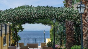 An outdoor seating area with wicker furniture, a view of the sea, and a decorative archway. - Imperial Hotel Tramontano (Sorrento)