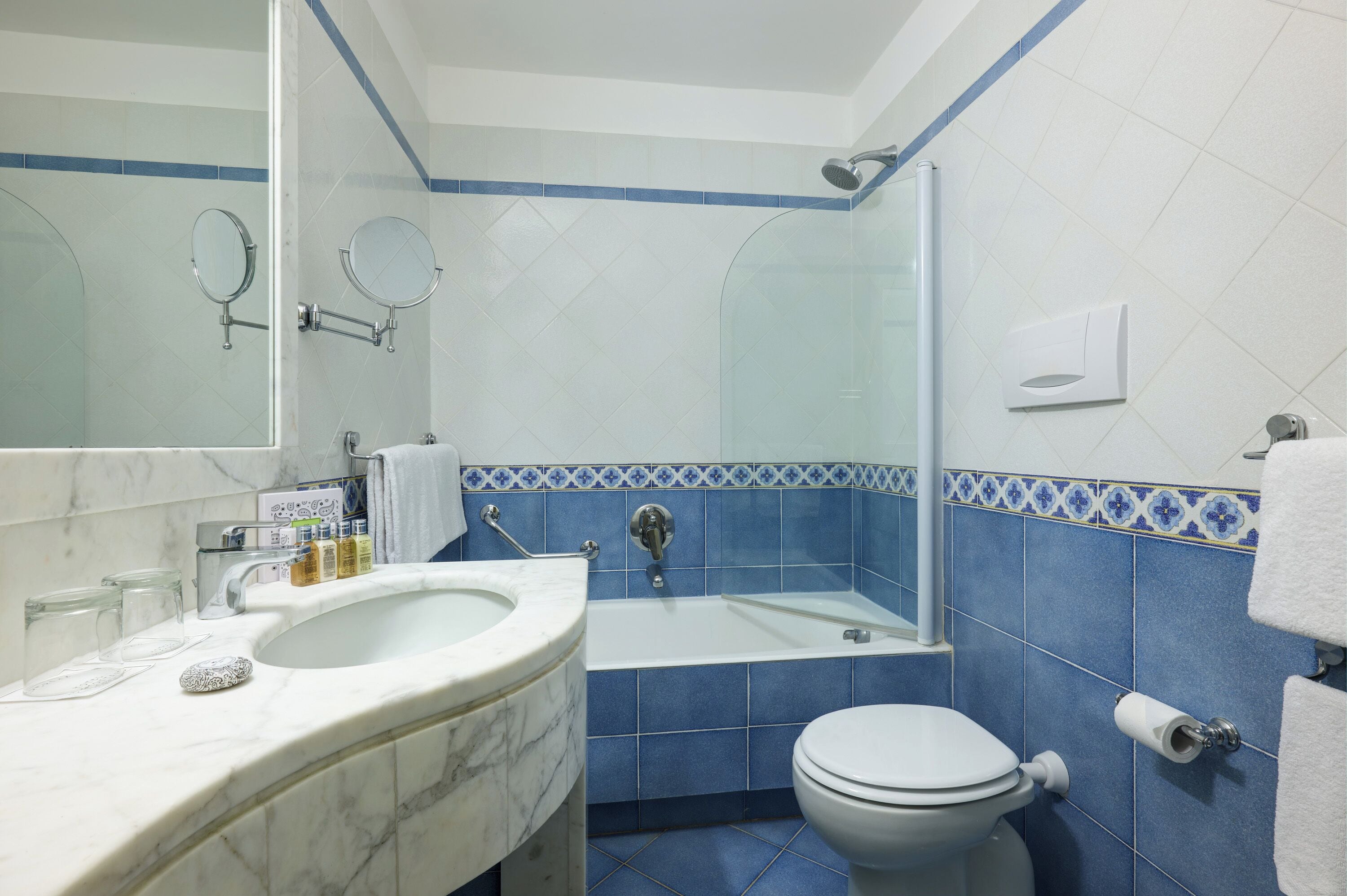 A bathroom with a marble sink, a bathtub, a toilet, and blue-tiled walls.