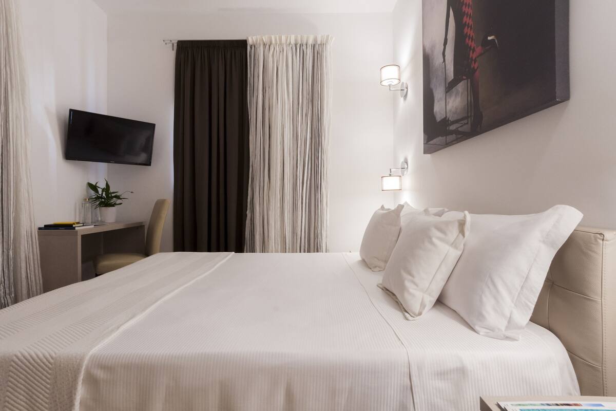 Hotellihuone, jossa on sänky, työpöytä, jossa on televisio, ja taulu seinällä.