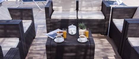 A sunlit outdoor seating area with wicker furniture and a table set for breakfast.