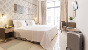 A hotel room with a large bed, bedside tables, a desk, a chair, a TV, and a window with curtains. - Alexandra Hotel (St. Julian's)