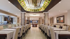 A spacious dining area with multiple tables and chairs, a central serving station, and a decorative ceiling. - Alexandra Hotel (St. Julian's)