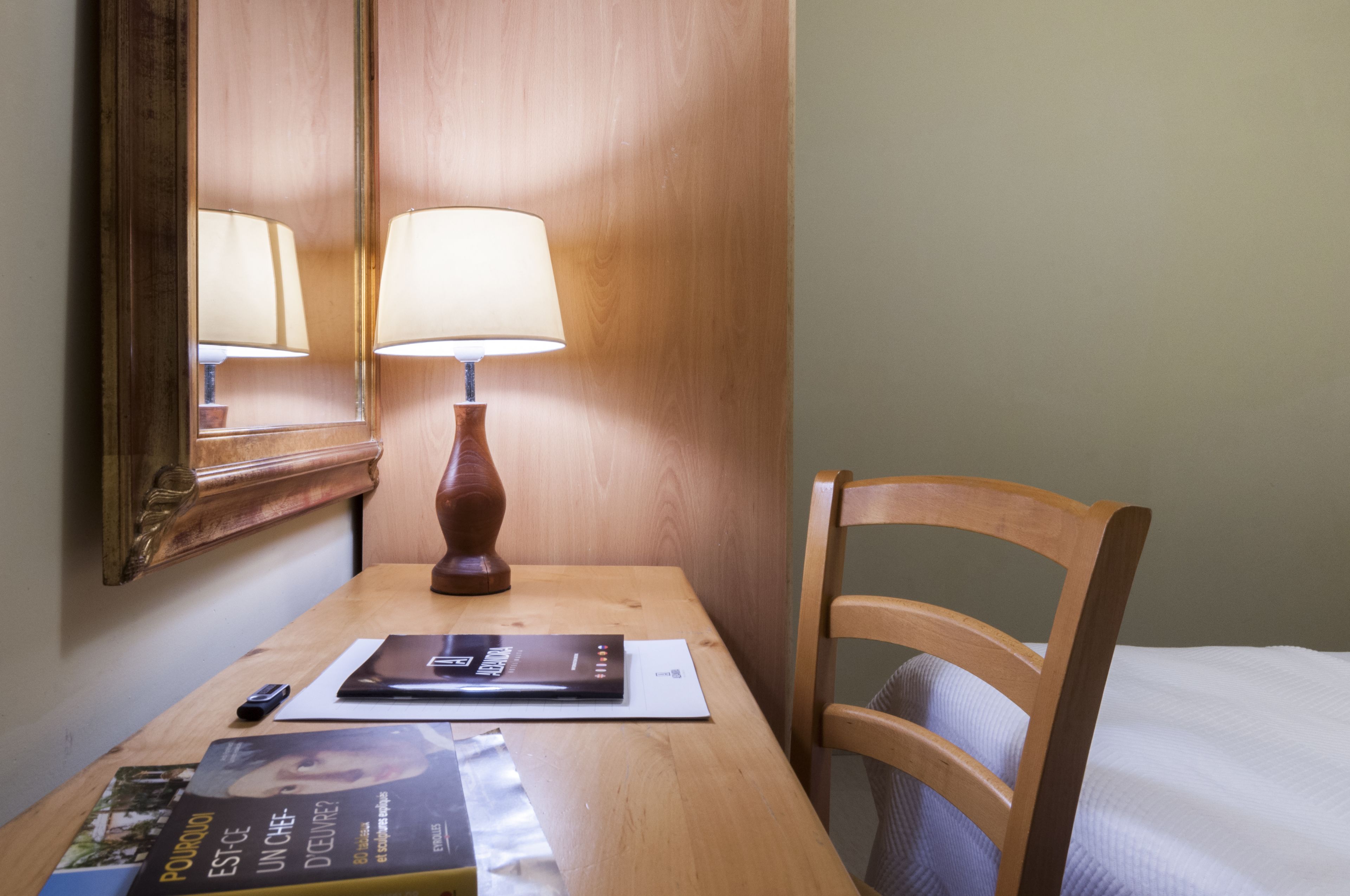 A wooden desk with a lamp, a chair, and a bed in a hotel room.