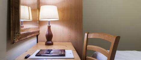 A wooden desk with a lamp, a chair, and a bed in a hotel room.