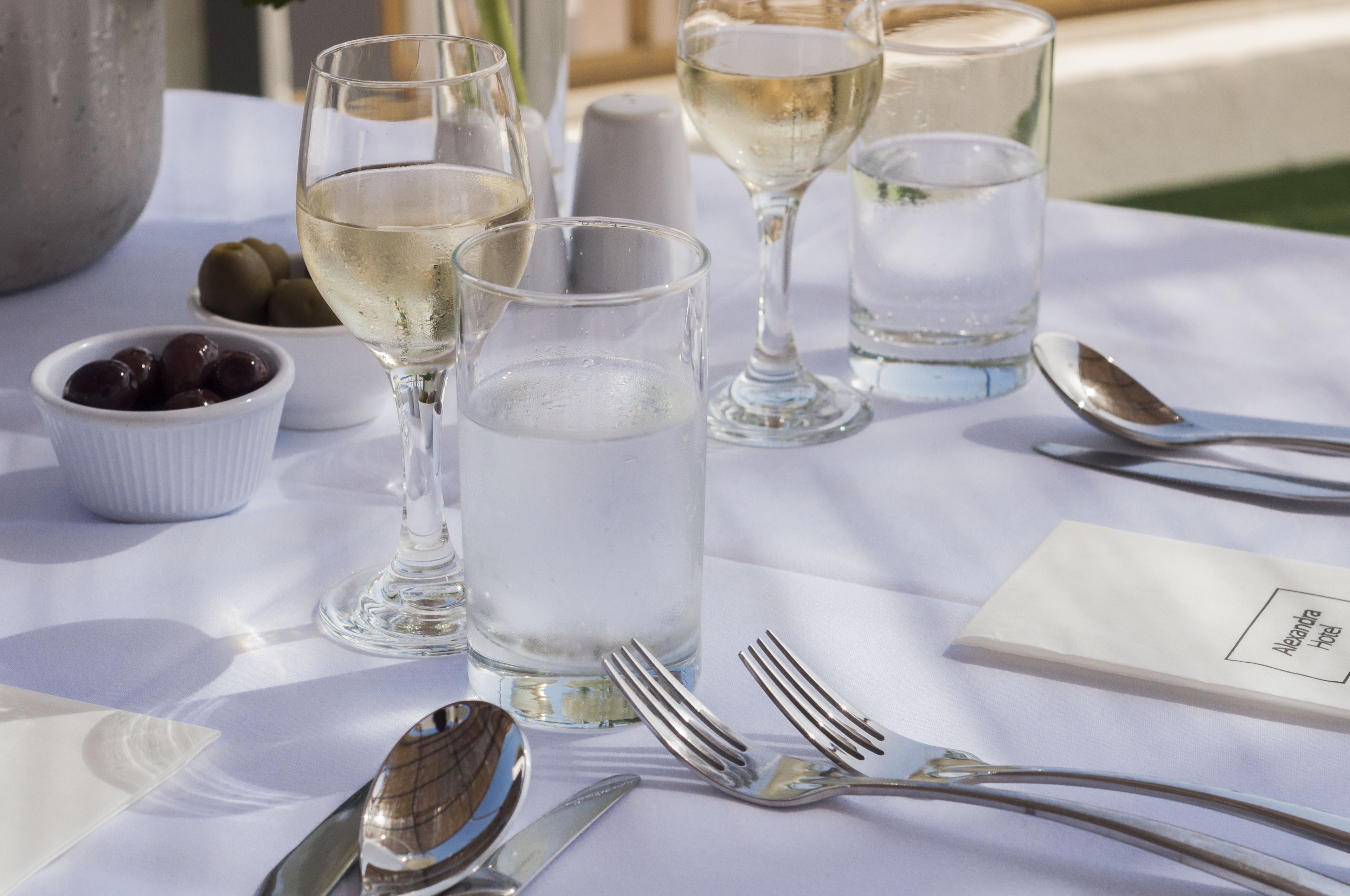Una mesa dispuesta con copas de vino, un bol de aceitunas y cubiertos, con un menú sobre la mesa.