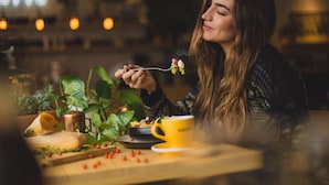 Una persona sentada en una mesa con una taza amarilla, un plato de comida y una planta al fondo.