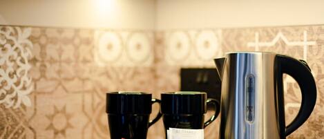 Una estación de café con un hervidor, dos tazas y cápsulas de café sobre una bandeja.
